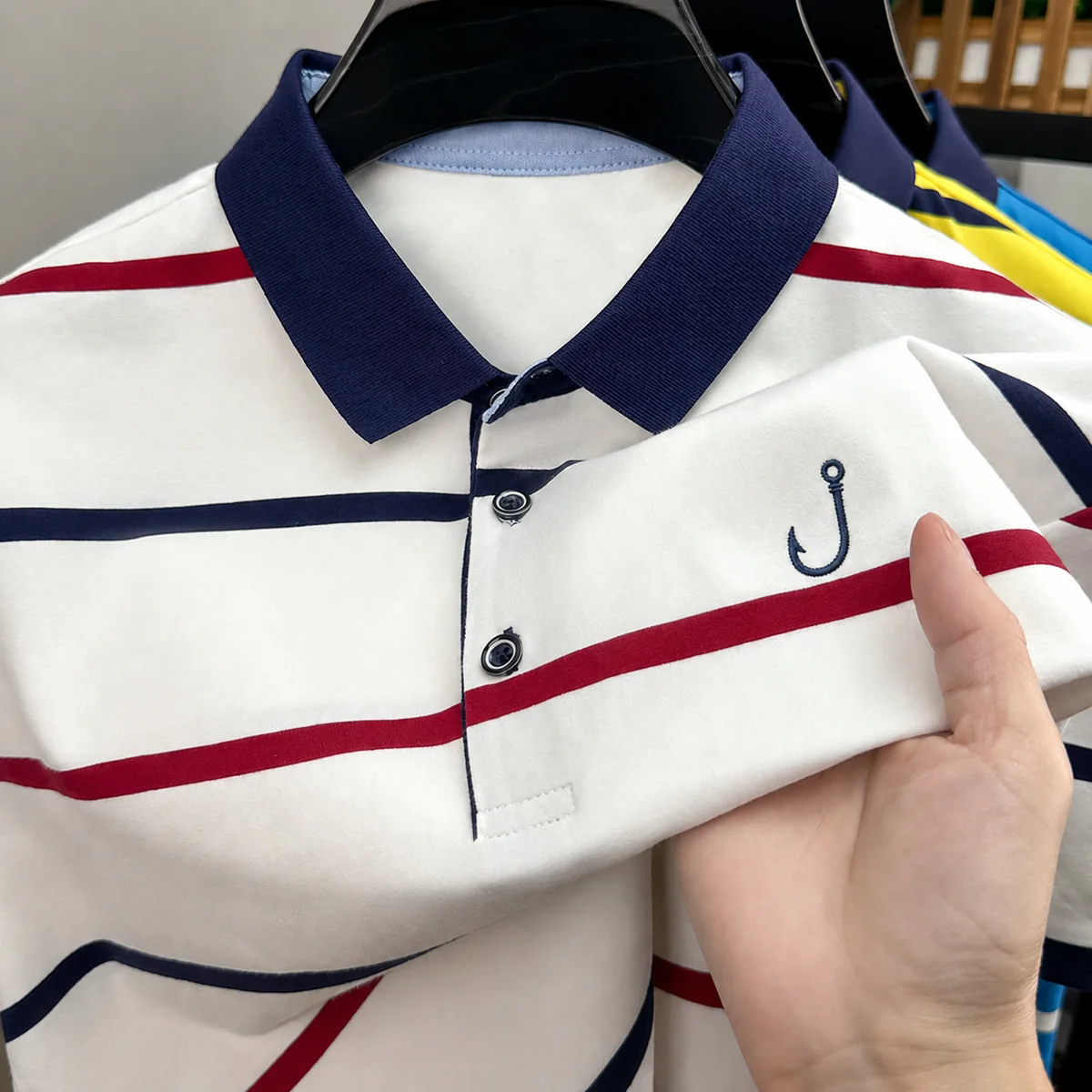 Close-up of a navy embroidered fish hook logo on a striped fishing polo shirt