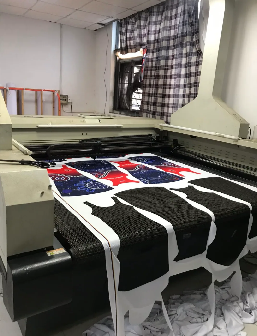 Automatic cutting machine cutting custom sublimated fishing polo fabric panels in a factory